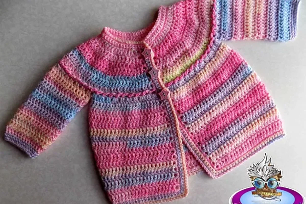 A Raised Shell Baby Outfit crocheted cardigan featuring pink, purple, blue, and yellow stripes with star-shaped buttons, displayed flat on a gray surface.