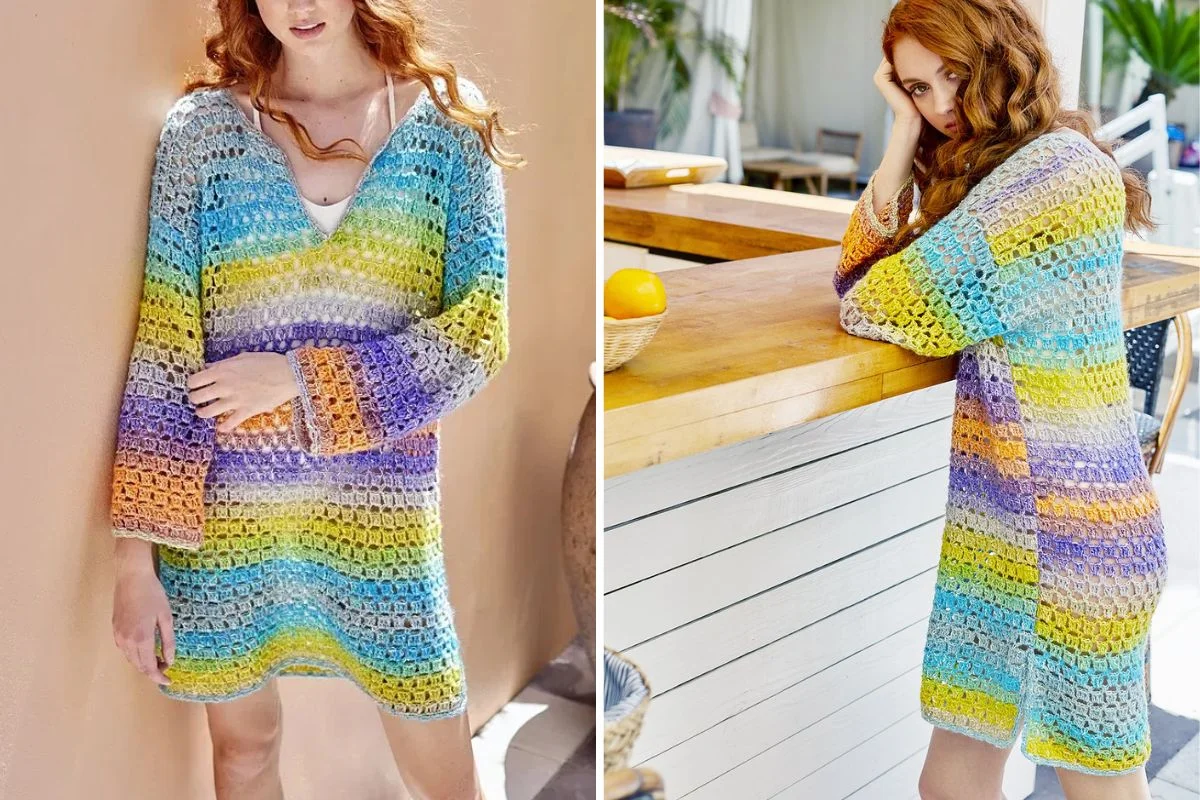 Woman wearing a loose, long-sleeved crochet dress with horizontal stripes in blue, green, yellow, orange, and purple tones, shown standing and leaning on a counter.