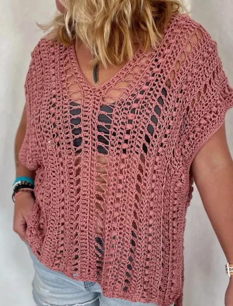 Person wearing a loose, pink crochet boho top over a black tank and light denim shorts, standing against a plain background—perfect inspiration for building your handmade wardrobe.