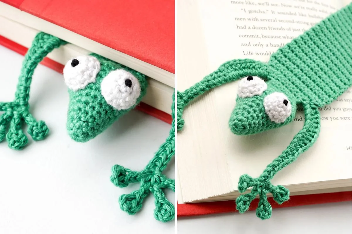 A crocheted green frog bookmark with bulging eyes lies across the pages of an open book, with its head and arms sticking out from the book's edge.