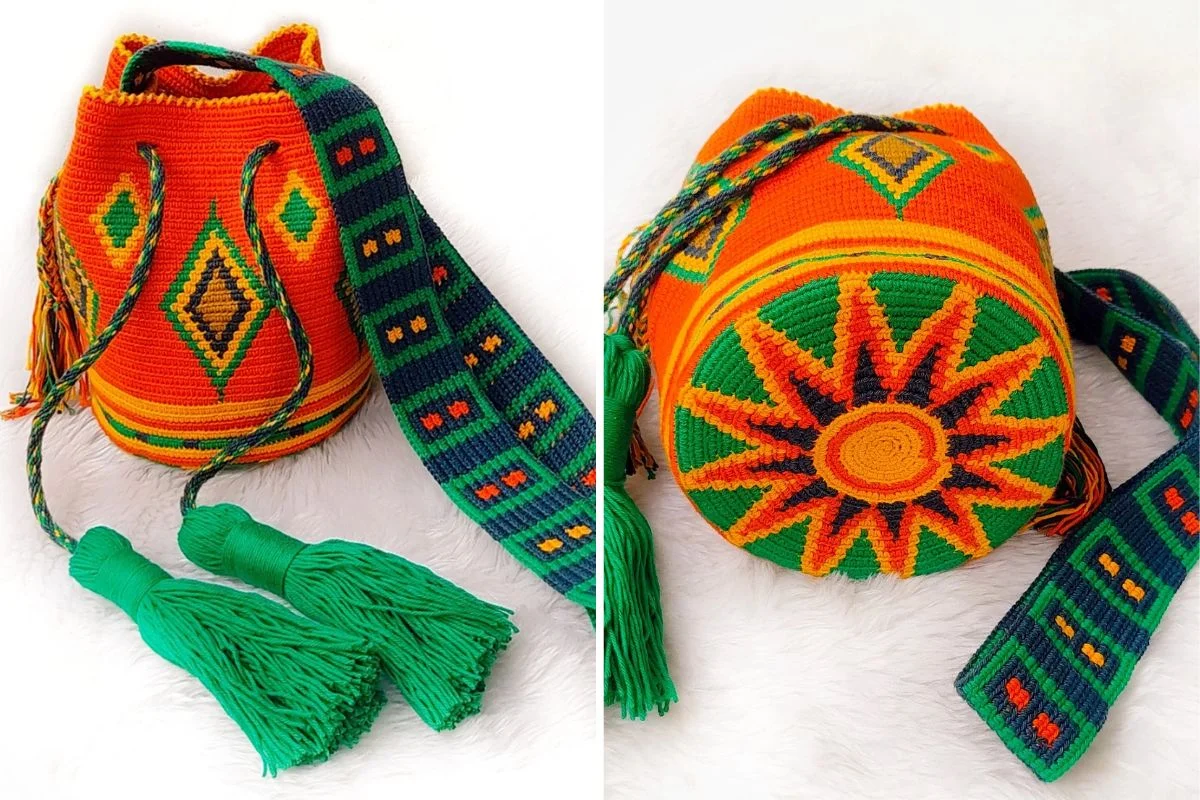 A handwoven orange, green, and yellow Mochila Bag with geometric patterns, thick braided strap, large tassels, and a sunburst diamond design on the round base, displayed on a white surface.
