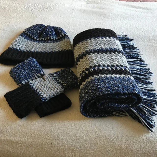 A set from Dusk Till Dawn featuring a striped hat, fringed scarf, and fingerless gloves in shades of blue, gray, and black, beautifully laid out on a light-colored surface.