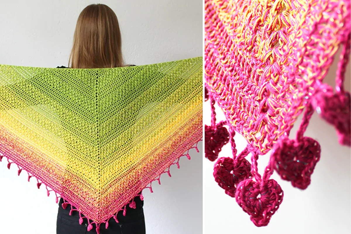 A person displays the lovely Luisa Shawl, a triangular crochet shawl with a gradient from green to yellow to pink, finished with pink heart-shaped tassels along the edge.