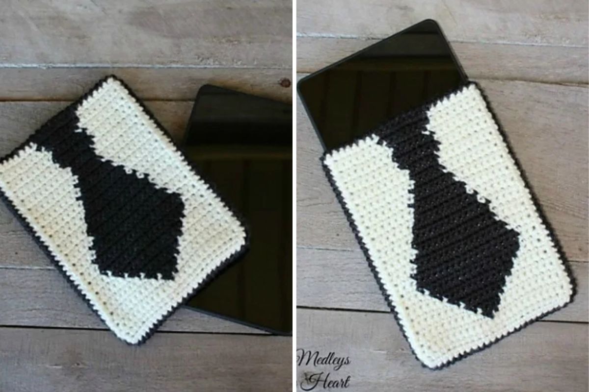 A crocheted tablet sleeve with a black tie design on a white background, shown with a tablet partially inside the sleeve, placed on a wooden surface.