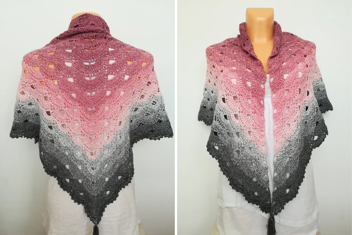 The Lovely Luisa Shawl is a crocheted triangular shawl displayed on a mannequin, featuring a gradient pattern transitioning from dark gray at the bottom to pink at the top.