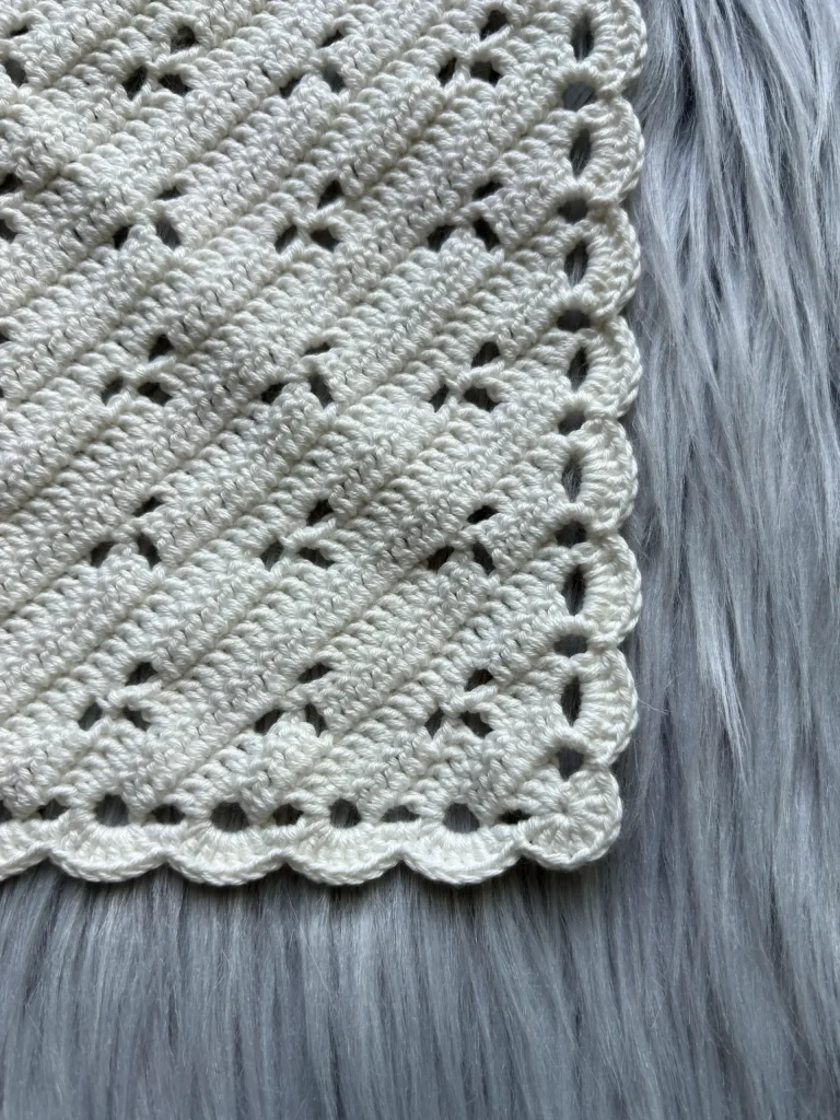 A close-up of a white crocheted fabric with a scalloped edge, placed on a light gray faux fur surface, perfect as inspiration for anyone searching for a crochet pumpkin pattern free.