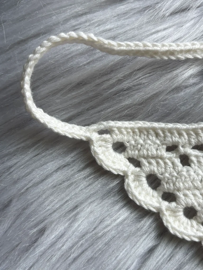 A close-up of a white crocheted piece with scalloped edges and a looped handle, placed on a gray faux fur surfaceโperfect for showcasing your latest project or complementing your favorite free crochet pumpkin pattern.