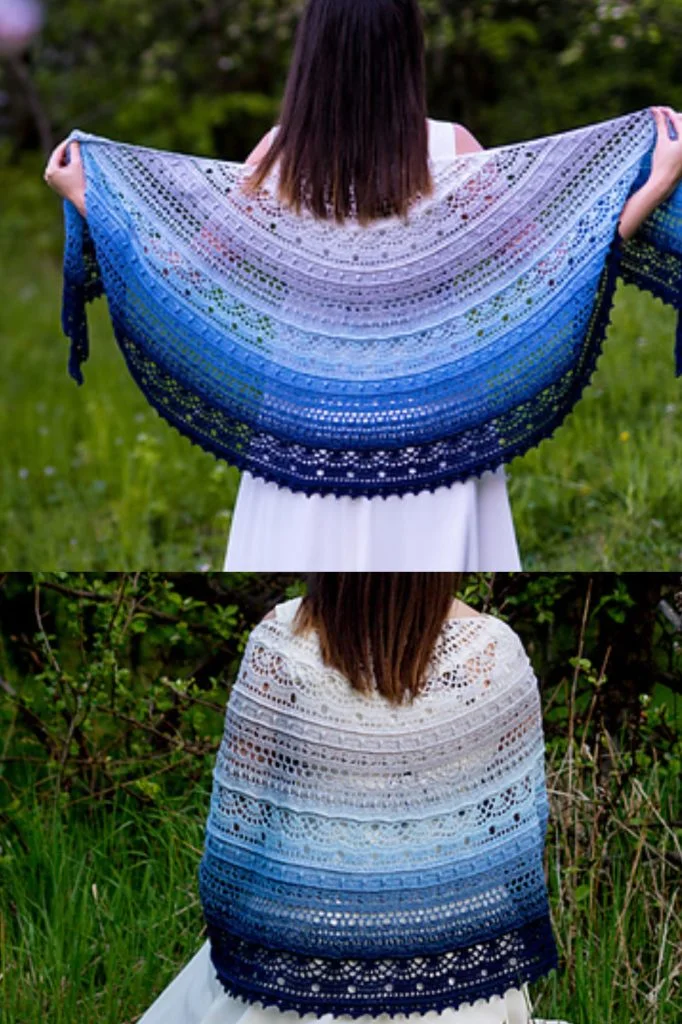 A person standing outdoors displays a large, semi-circular crocheted shawl in gradient blue, white, and navy tones, shown both spread wide and draped over their shoulders.