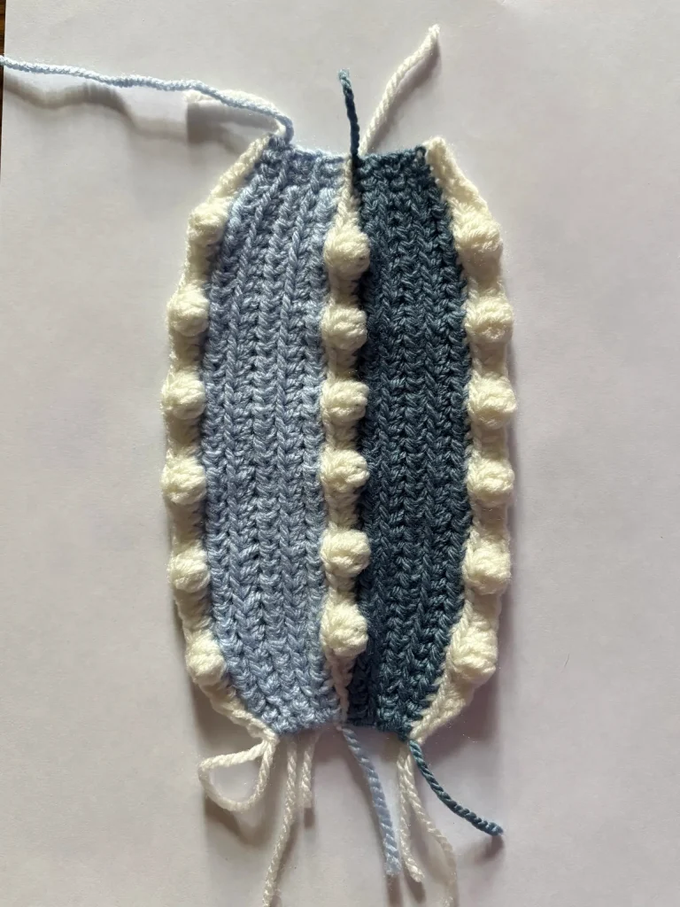 A crochet swatch with alternating light blue and dark blue vertical stripes, edged with a row of raised white bobbles, is displayed on a white backgroundโa beautiful piece that would pair perfectly with any free crochet pumpkin pattern or whimsical Toadstool Gnome project.