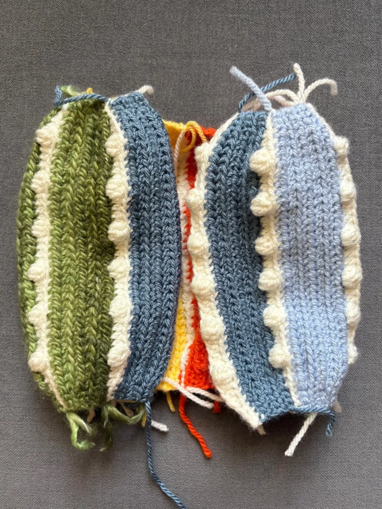 Two crocheted pieces in green and blue with white textured edges, sewn together with visible yarn ends, lying on a gray surfaceโperfect for practicing your pumpkin crochet pattern or adding whimsical touches like those found in Toadstool Gnome designs.