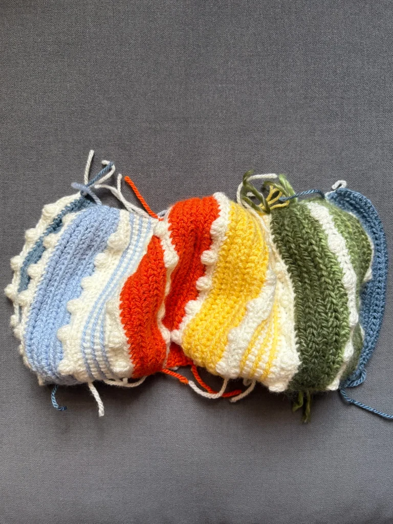 A swatch of crocheted fabric with wavy stripes in blue, red, yellow, green, and white yarn on a gray backgroundโperfect inspiration for your next pumpkin crochet pattern or whimsical projects like a Toadstool Gnome.