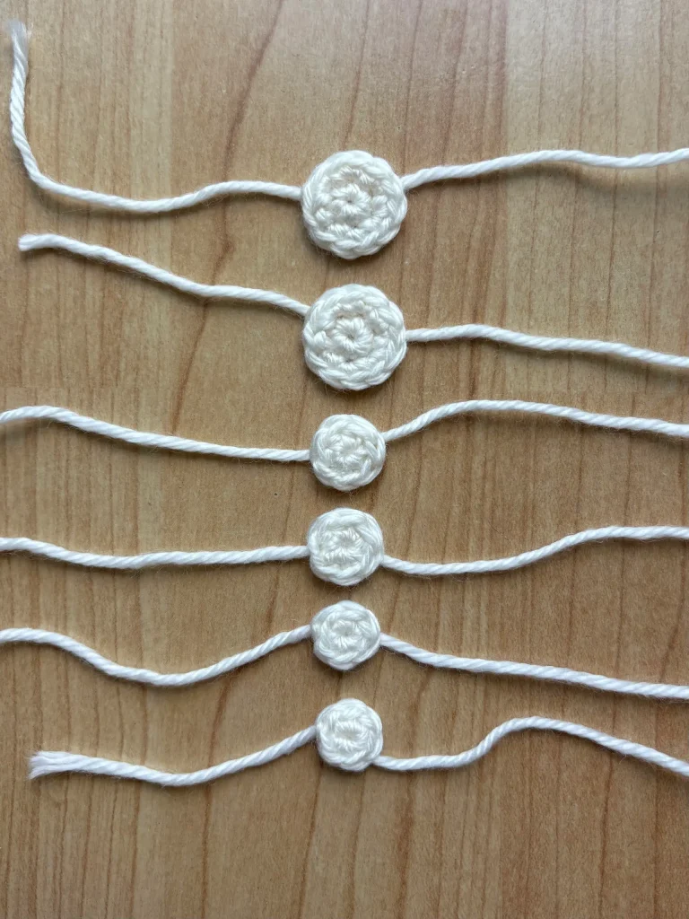 Six crocheted circles of varying sizes, each attached to strings on both sides, are displayed in a vertical row on a wooden surfaceโan arrangement that would beautifully complement your favorite pumpkin crochet pattern or even a whimsical Toadstool Gnome creation.