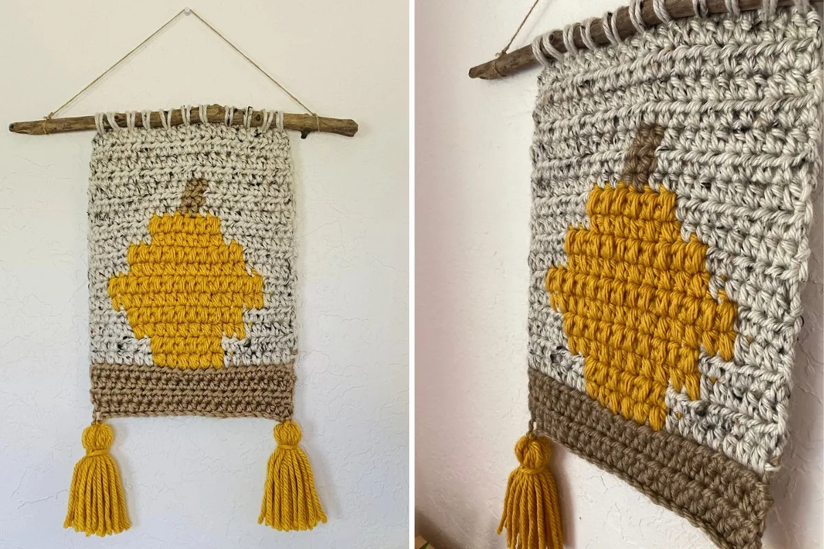 A crocheted wall hanging with a yellow pumpkin design, two yellow tassels at the bottom, and a wooden branch for hanging.