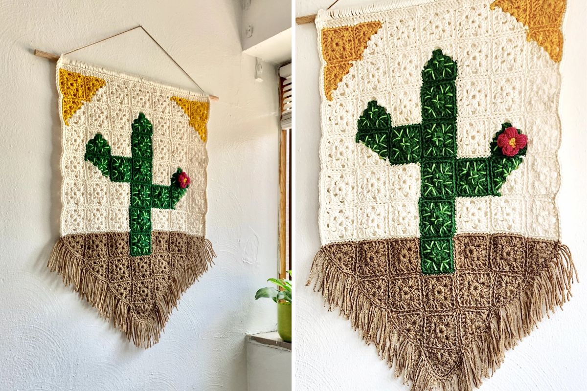 A crocheted wall swag featuring a saguaro cactus design, brown fringe at the bottom, a yellow sun in the corner, and a small red flower on one cactus arm. The piece hangs beautifully from a wooden rod.