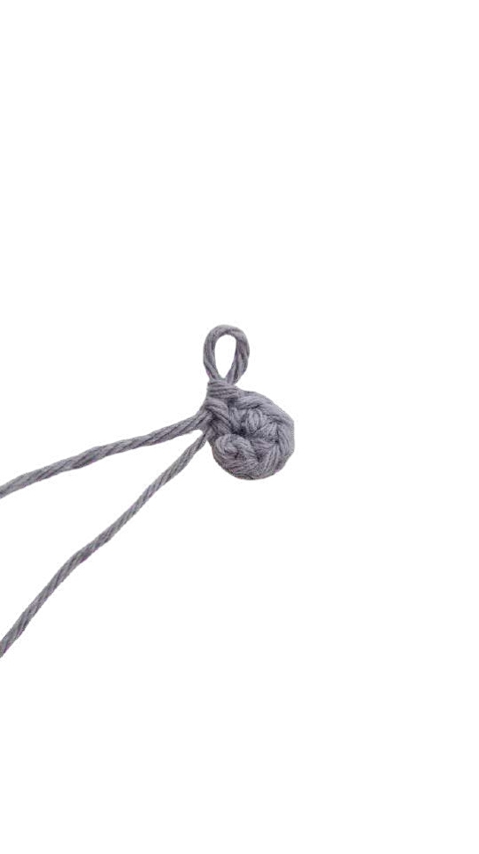 A small grey crochet circle used in an elephant amigurumi, featuring a loop and two loose yarn tails.