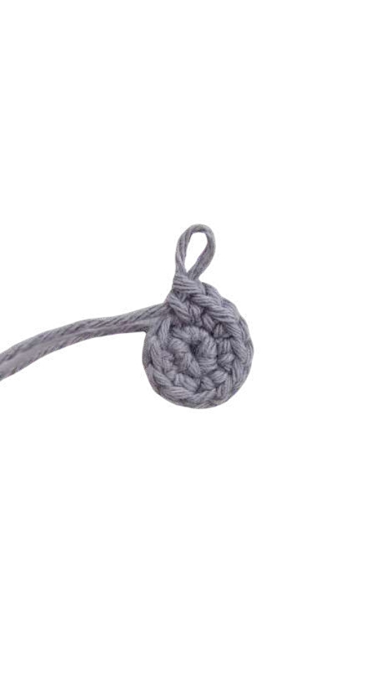 A small circular piece of gray crochet, resembling a base for an elephant amigurumi, with a yarn loop extending from the top edge.