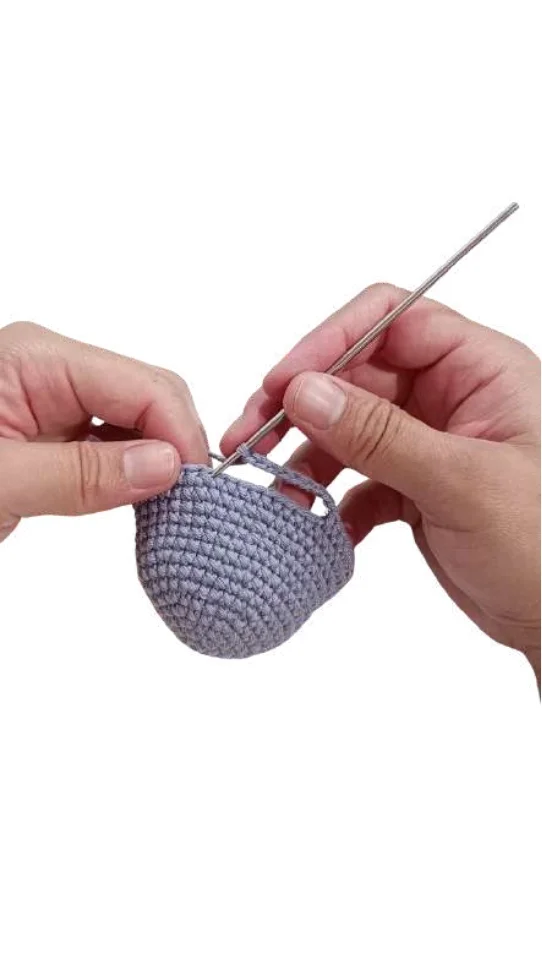 Hands holding a crochet hook and a partially completed grey circular piece for an elephant amigurumi.