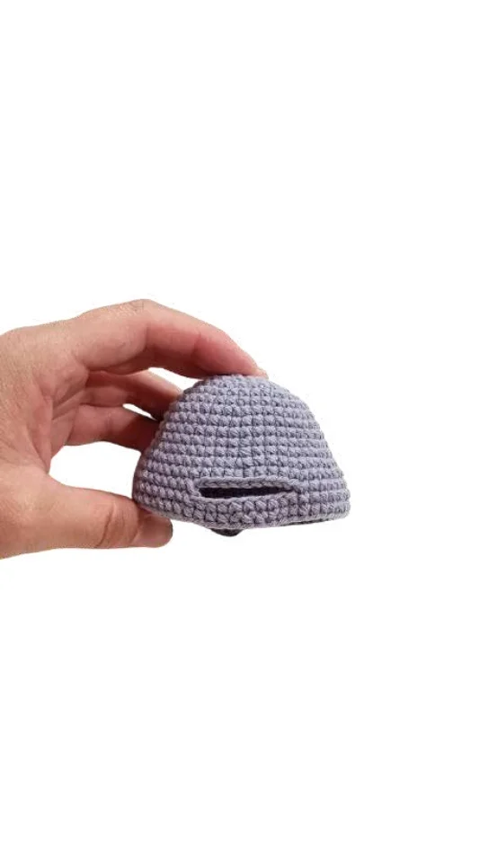 A hand holding a small, dome-shaped lavender crochet pumpkin pattern cover with a horizontal slit.
