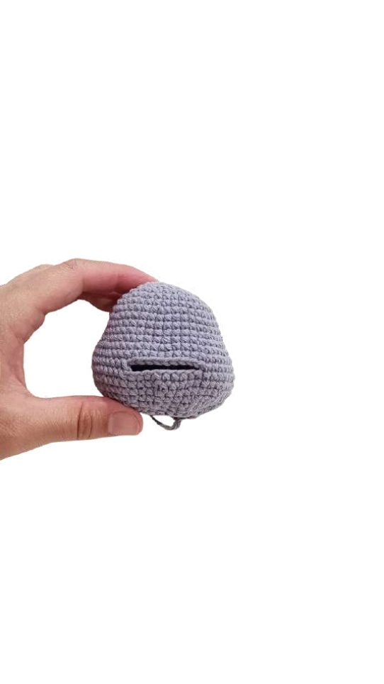 A hand holding a small, gray, bell-shaped object from a free crochet pumpkin pattern with a horizontal slit.