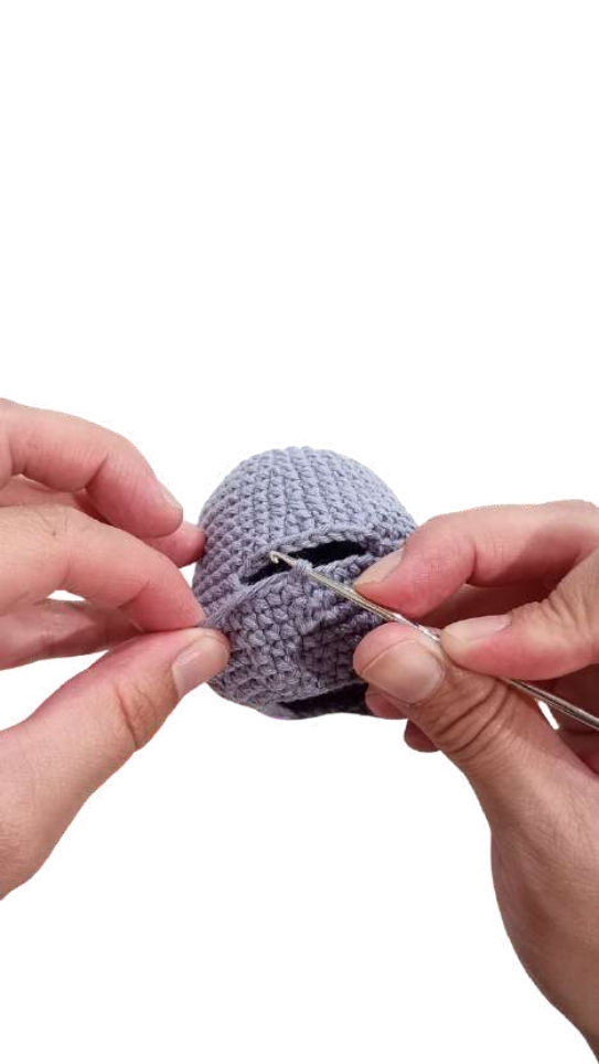 Hands using a metal crochet hook to work on a grey, dome-shaped elephant amigurumi.