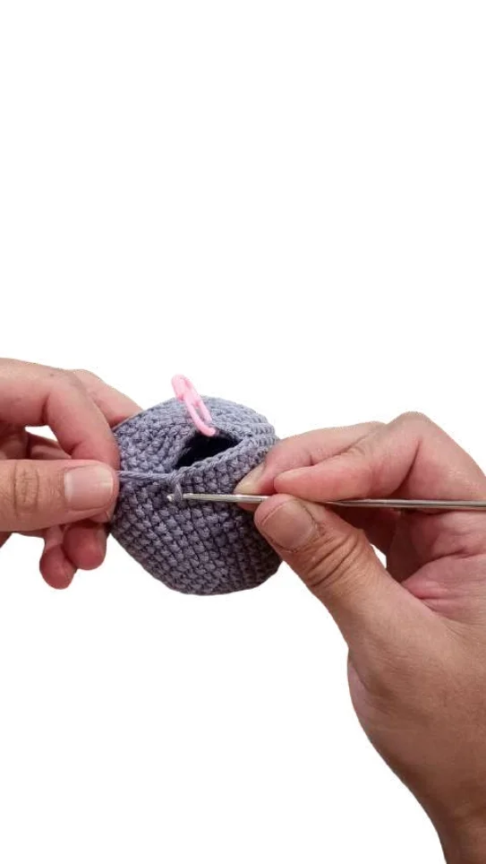Hands crocheting a small, round, grey piece for an elephant amigurumi using a metal hook and a pink stitch marker.