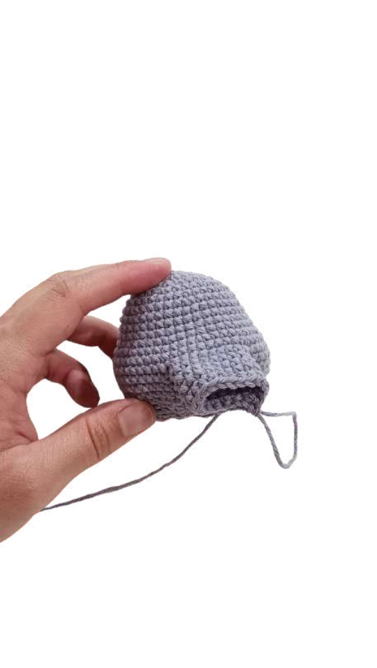 A hand holding a small, dome-shaped piece of grey crochet work for an elephant amigurumi.