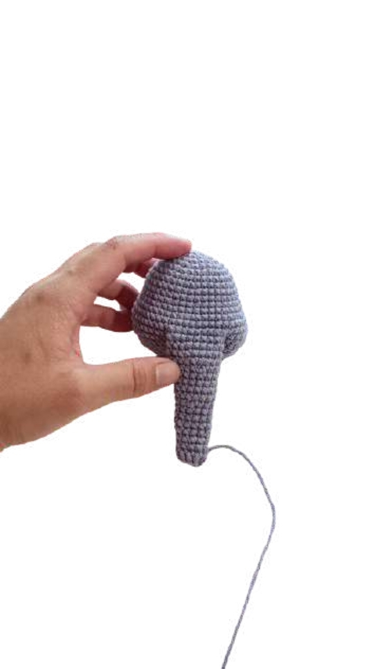 A hand holding a crocheted gray trunk piece for an elephant amigurumi.