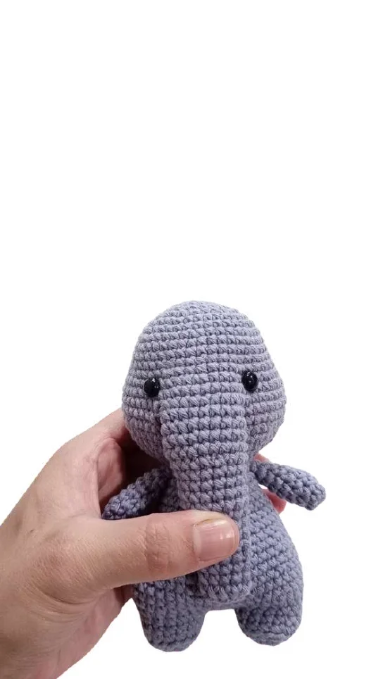 A hand holds a small, grey crocheted elephant toy, a charming companion to our free crochet pumpkin pattern.