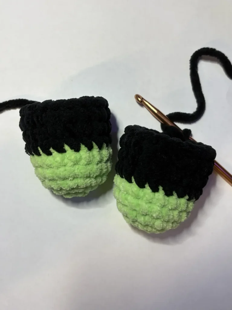 Two crocheted pieces in black and neon green yarn for a Frankenstein plushie, one with a crochet hook inserted.