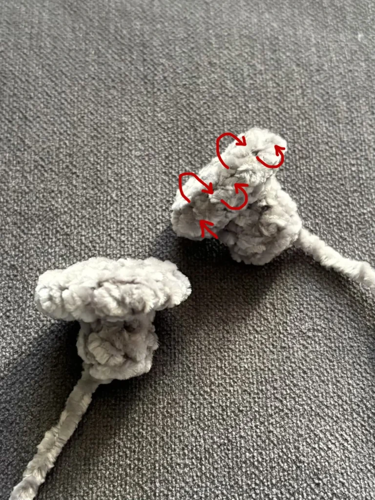 Two grey yarn shapes, one with red arrows pointing to the top section to indicate a folding direction for a crochet Frankenstein amigurumi pattern.