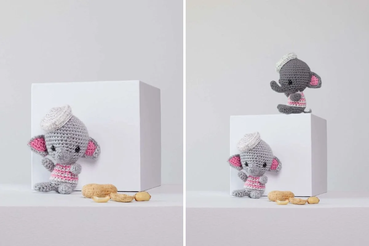 Two Mini Love Elephant amigurumi figures in pink-and-white striped shirts and white hats are positioned next to a white cube and several peanuts.