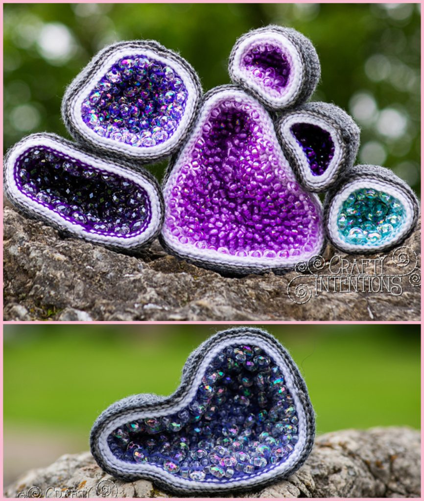 Crocheted, bead-filled geodes in shades of purple and teal resting on a rock, inspired by unique crochet geode patterns.