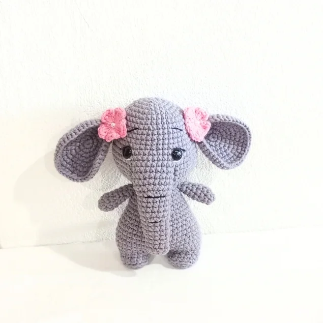 Crocheted gray elephant amigurumi plush toy with small pink flowers on its ears.