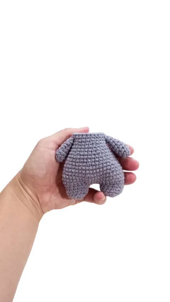 A hand holding a small, gray elephant amigurumi doll body.