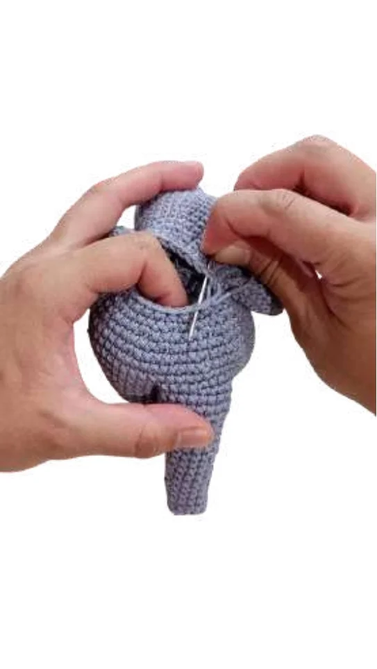 Hands sewing a grey crochet pumpkin pattern piece with a needle and thread.