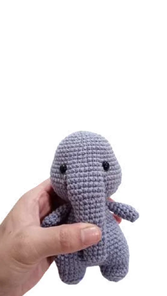 A hand holds a small, grey elephant amigurumi toy.