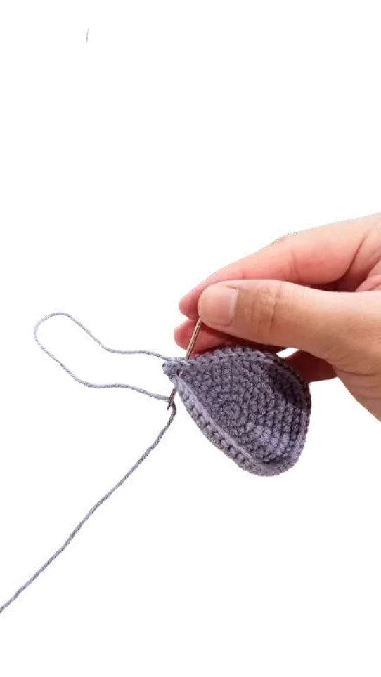 A hand using a metal needle to sew through a piece of gray crocheted fabric while following a crochet pumpkin pattern.
