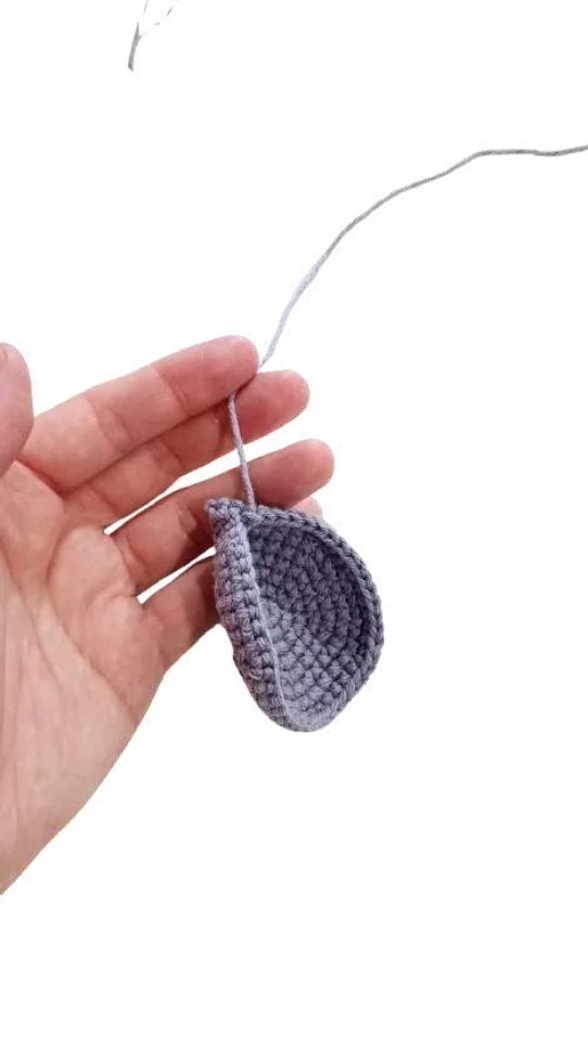 A hand holds a grey, bowl-shaped piece of crochet work attached to a length of yarn, created using a free crochet pumpkin pattern.