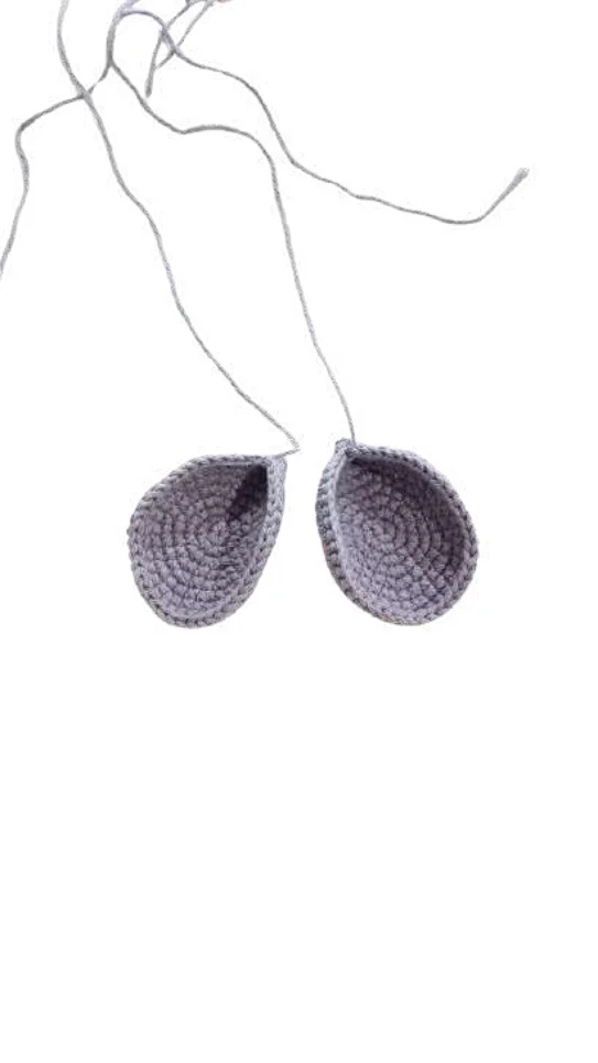 Two grey crocheted animal ears with long yarn tails, designed as an embellishment for a crochet pumpkin pattern.