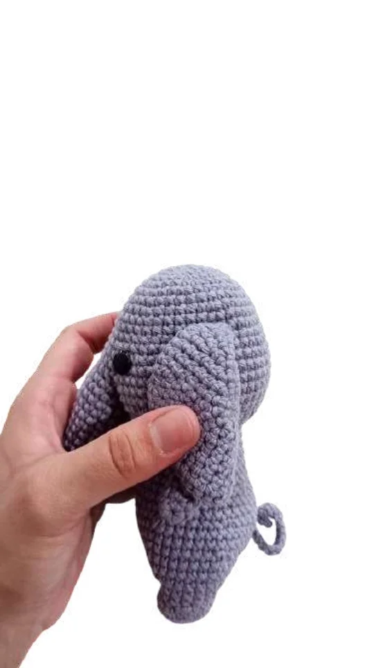 A hand holds a small, gray elephant amigurumi toy.