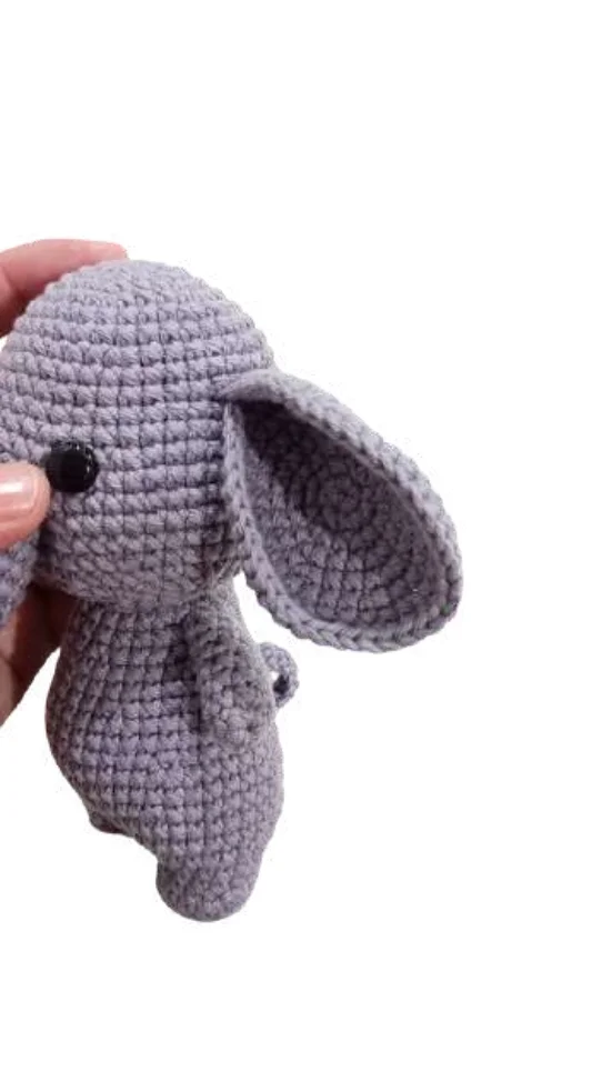 A hand holding a small, grey elephant amigurumi.
