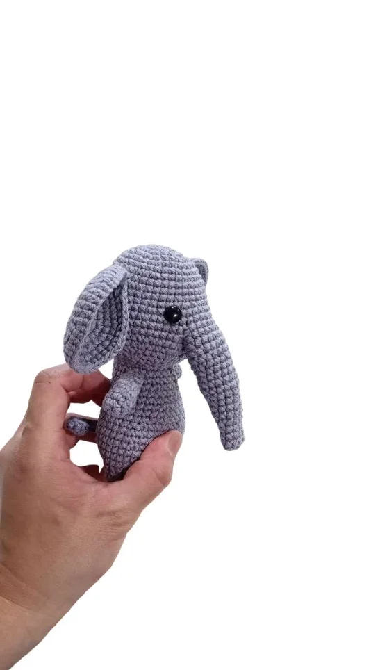 A hand holds a small, grey crocheted elephant toy, a cute alternative to a classic crochet pumpkin pattern.