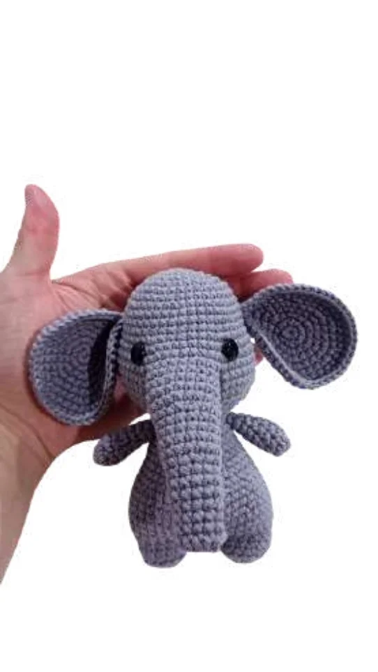 A small, gray elephant amigurumi toy held in a person’s hand.