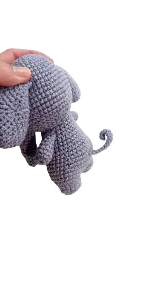 A hand holding a grey, crocheted elephant toy next to a crochet pumpkin pattern.