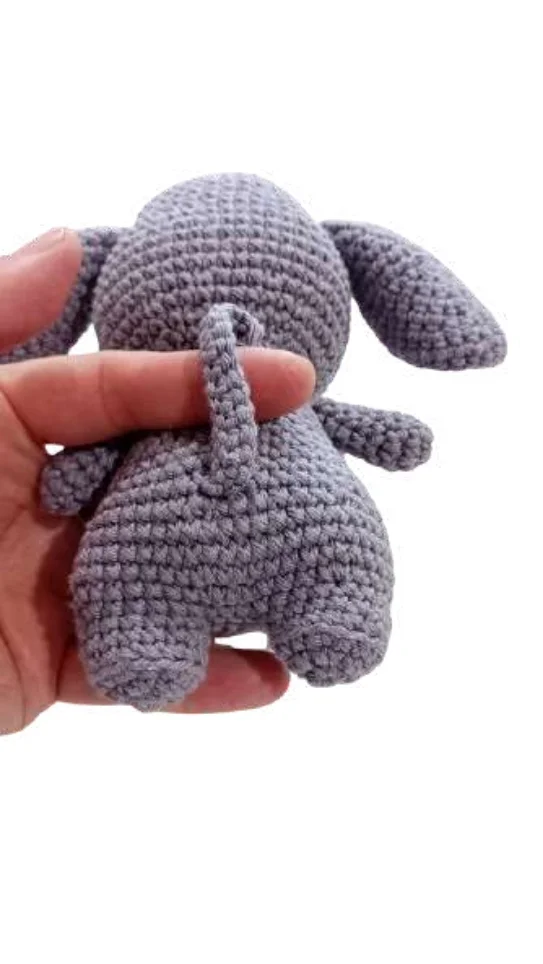 Hand holding a small, gray crochet pumpkin pattern toy viewed from the back.