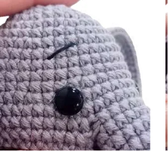 Close-up of a grey elephant amigurumi with a black eye and a stitched eyebrow.