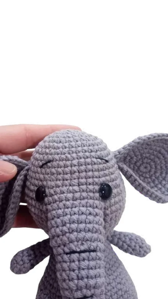 A hand holds a small, grey elephant amigurumi crochet toy.