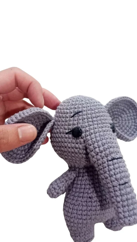 A hand adjusts the ear of a small, grey crocheted elephant toy next to a free crochet pumpkin pattern.