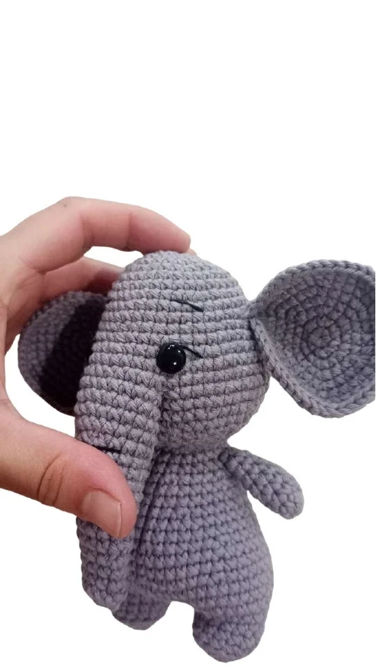 A hand holds a small, grey elephant amigurumi toy.