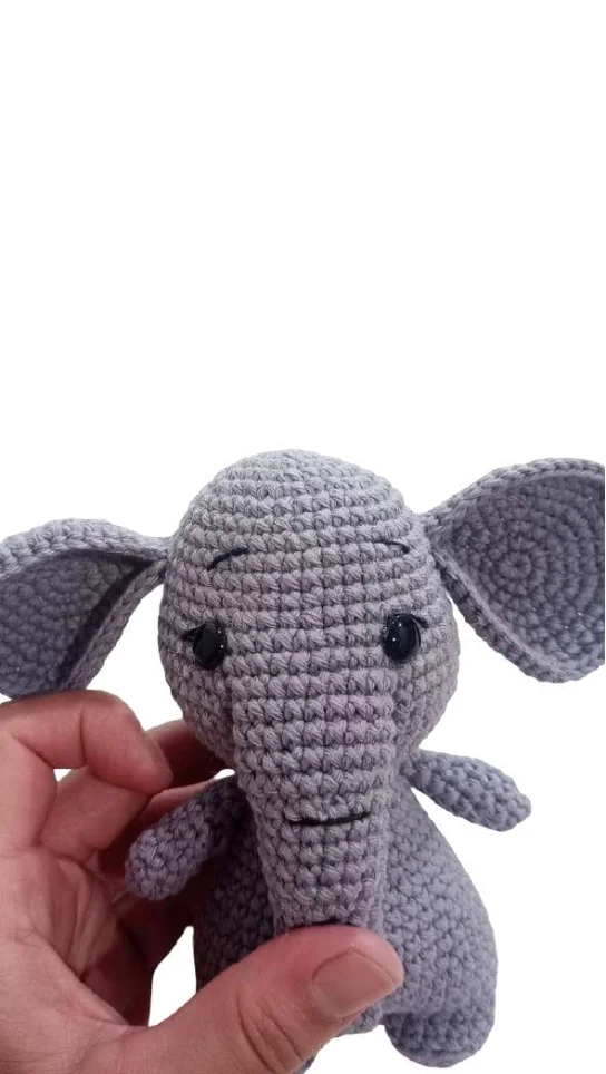 Hand holding a small, gray elephant amigurumi toy.
